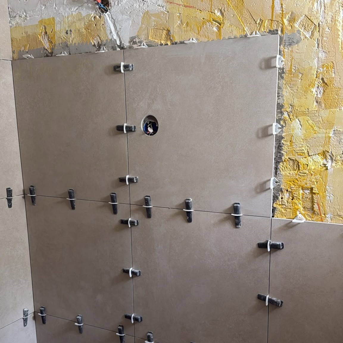 Grote wandtegels tijdens het plaatsen, met tegelclips voor een vlakke wand