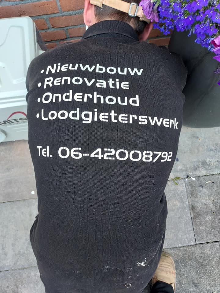 Rugzijde van een werkshirt met de tekst Nieuwbouw, Renovatie, Onderhoud, Loodgieterswerk en het telefoonnummer