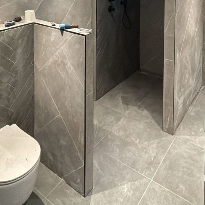 Opgeleverde badkamer met grijze tegels in marmerlook, hangtoilet en douchewand