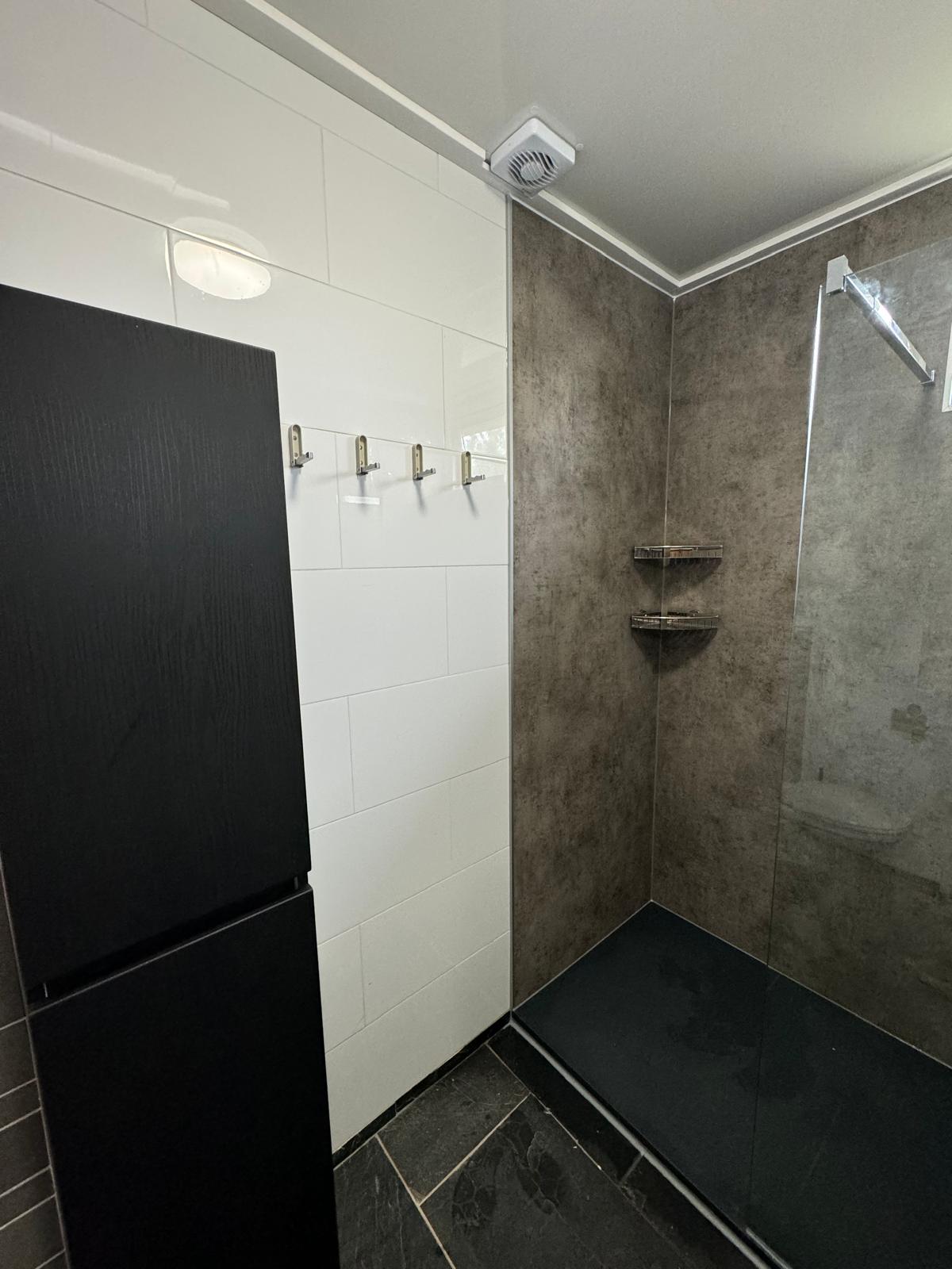 Opgeleverde douche met wandpanelen in betonlook, witte tegels en een donkere vloer